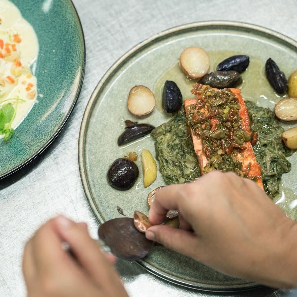 Main déposant un coquillage sur une assiette de poisson, épinards et pommes grenaille